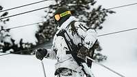 Ein Soldat in Schneetarnuniform fährt auf Skiern einen verschneiten Hang hinunter.