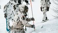 Ein Soldat in Schneetarnuniform sticht mit einer über zwei Meter langen dünnen Sonde in den Schnee.