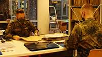 Zwei Soldaten mit Mund-Nasenschutz sitzen in einem Büro an einem Schreibtisch. Vor einem liegen schwarze Röntgenaufnahmen.