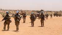 Bundeswehr soldiers with weapons and blue UN caps on patrol in a desert landscape