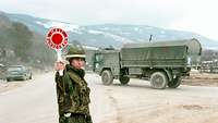 Soldier stands on a dirt road and holds up a red Bundeswehr signal trowel