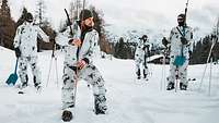 Vier Soldaten in Schneetarnuniform stehen auf einer Schneefläche verteilt.