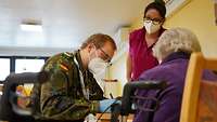 Ein Bundeswehr-Arzt führt ein Impfgespräch mit einer Bewohnerin einer Senioreneinrichtung durch.