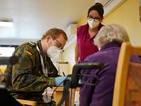 Ein Bundeswehr-Arzt führt ein Impfgespräch mit einer Bewohnerin einer Senioreneinrichtung durch.
