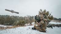 Ein grauer Lenkflugkörper nach dem Abschuss aus einer Panzerabwehrwaffe. Der Schütze sitzt neben der Zieloptik im Schnee. 