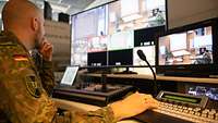 Ein Soldat sitzt vor einem Mischpult und mehreren Bildschirmen.
