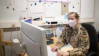 Eine Soldatin trägt einen Mund-Nasen-Schutz und arbeitet an ihrem Computer