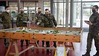 Soldaten stehen an einem Tisch, auf dem modellhaft Geländeabschnitte dargestellt sind.
