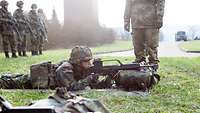 Ein Soldat liegt auf der Wiese mit einem Gewehr, das auf seinem Marschgepäck aufliegt.