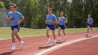 Soldaten in blauer Sportbekleidung laufen auf einer roten Tartanbahn eines Sportplatzes entlang.