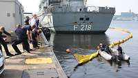 Feuerwehrleute auf einer Pier ziehen einen Sperrkörper auf dem Wasser zu sich