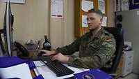 Ein Soldat sitzt im Büro und arbeitet am Computer