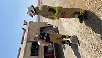 Tom steht in voller Feuerwehrmontur vor dem Feuerwehrmann und sieht ihn aufmerksam an. 