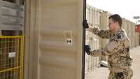 Ein Soldat öffnet einen ockerfarbenen Container, im Hintergrund weitere Container