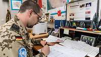 Ein Soldat sitzt im Büro am Schreibtisch und schreibt etwas in den Tischkalender