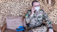 Ein Soldat sitzt auf einem Sofa und telefoniert, neben ihm liegt ein hellblaues Barett
