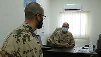Zwei Soldaten sitzen einander in einem Büro gegenüber, beide tragen Mund-Nasen-Schutz