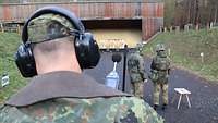 Ein Soldat mit Gehörschutz und einem Lärm-Messgerät steht auf einer Standortschießanlage hinter zwei Soldaten. 