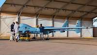 Drei Personen stehen am unbemannten Luftfahrzeug, welches sich in einem Hangar befindet