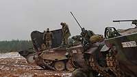 Mehrere Schützenpanzer stehen in einer Reihe, zwei Soldaten stehen auf der Motorklappe eines Panzers