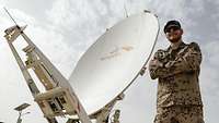 Ein Soldat steht in Wüstentarnuniform vor einer Satellitenschüssel