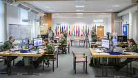 Several soldiers are sitting at their workplaces separated by Plexiglas screens.