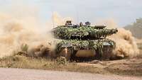 Ein Kampfpanzer Leopard fährt durch das Gelände und wirbelt Staub auf