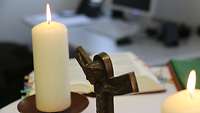 Ein Kreuz mit Kerzen vor einer Bibel.