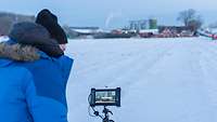 Der Kameramann macht in aller Frühe mitten in der Schneelandschaft Aufnahmen vom Bauernhof
