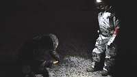 Im Dunkeln stehen zwei Soldaten auf dem Sprengfeld. Mittig strahlt der Lichtkegel einer Kopflampe auf den Boden.