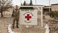 Eine Soldatin steht neben einem Schild mit der Aufschrift „German Field Hospital“, im Hintergrund Flachbauten