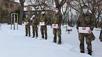 Zwei Soldatinnen und drei Soldaten stehen vor der Klinik im Schnee. In den Händen halten Sie eine Tafel Pralinen.