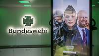 Eine digitale Werbestele zeigt bundeswehrkarriere.de, dahinter das Logo der Bundeswehr beleuchtet an einer Wand