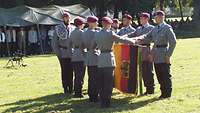 Sechs Soldaten stehen an einer gesenkten Truppenfahne. Jeweils eine Hand liegt auf der Fahnenstange.