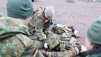 Ein Soldat liegt am Boden, ein anderer hockt neben ihm. Zwei Soldaten schauen zu.