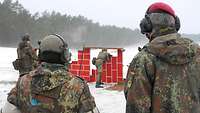 An einer roten, provisorischen Mauer lehnt ein Soldat und schießt, drei Soldaten schauen ihm zu.