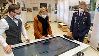 Drei Personen schauen auf einen Multimediatisch in einer Ausstellung