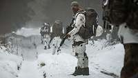 Soldaten in Schneetarn laufen hintereinander durch einen verschneiten Wald, der letzte Soldat dreht sich um.