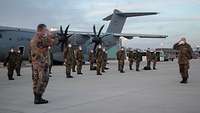 Soldatinnen und Soldaten stehen in drei Reihen mit weiten Abständen vor einem Airbus A400M, zwei davon salutieren davor.