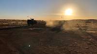 Drei Fahrzeuge der Objektschutzkompanie fahren durch die Wüste, die Sonne steht im Hintergrund tief am Himmel