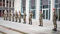 Zehn Soldaten stehen vor einem modernen Gebäude in einer Reihe nebeneinander.