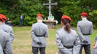 Soldaten mit roten Baretten stehen auf einer Wiese, vor ihnen ein Militärpfarrer und ein Feldkreuz.