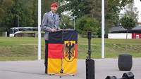 Ein Offizier spricht an einem Pult. Es ist umhüllt von einer Bundesdienstflagge mit dem Bundesadler.