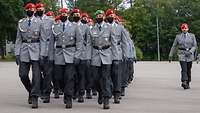 Soldaten in Dienstanzug mit rotem Barett marschieren in Formation über einen Platz.