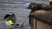 Ein Soldat zieht einen Ertrinkenden im Wasser mit sich, während ein anderer an Land ihm eine Stange reicht.