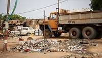 Müllansammlungen und defekte Autos auf einer unbefestigten Straße.