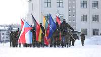 Mehrere Soldaten marschieren in Formation mit Flaggen der Partnernationen auf den Paradeplatz