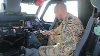 Ein Soldat sitzt im Cockpit des A400M und blickt auf einen Monitor. Er analysiert die Daten