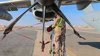 Ein Soldat steht auf einer Leiter am Propeller des A400M und hält eine rote Abdeckung. Ein anderer Soldat hält die Leiter