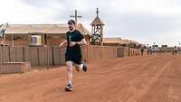 Ein Soldat joggt auf einer Straße im Feldlager, im Hintergrund steht die Feldkirche
